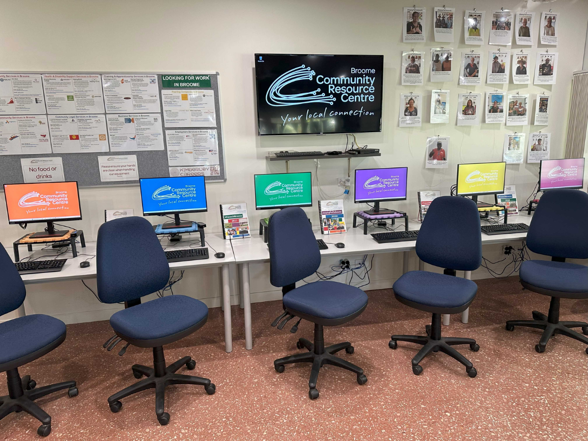 Row of computers with rainbow coloured screens and swivel chairs in a room. 