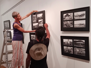 HEADING: Historical photographic exhibition in Mission Beach - Echo of the past. IMAGE: Two ladies hanging exhibition artwork.