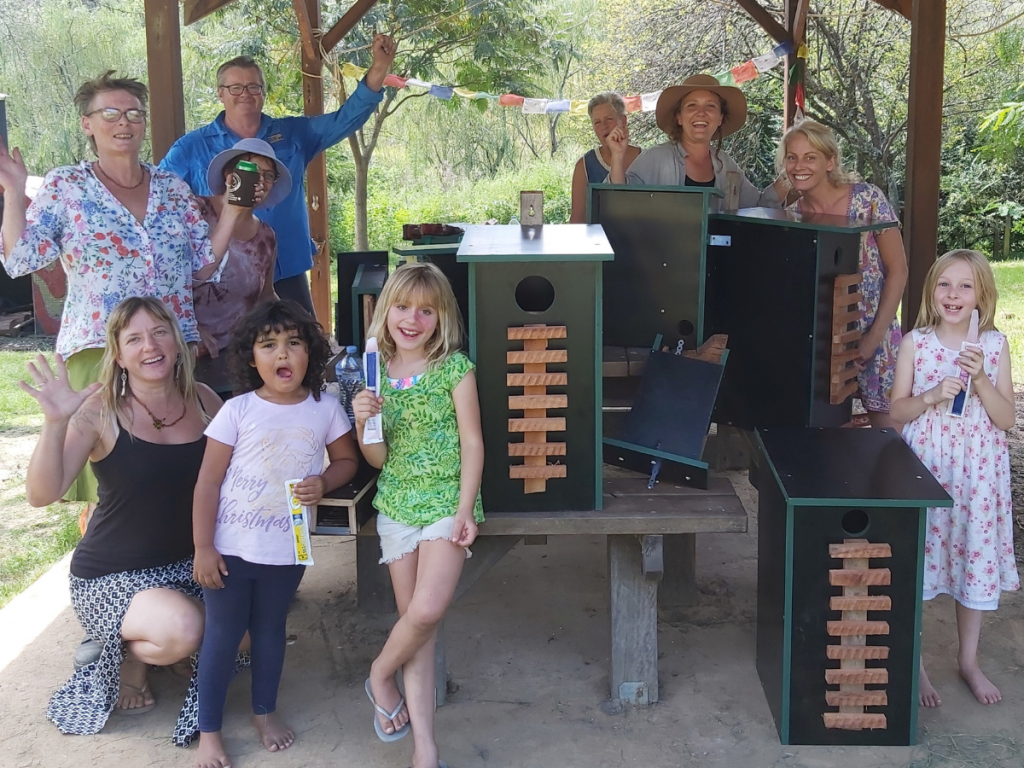 HEADING: Rural communities given a .7 million boost. IMAGE: Group of people smile and wave at camera with birdfeeders.