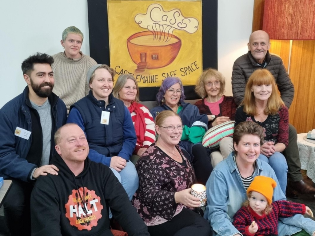 Group of people seated, smiling for the camera in front of a sign. 