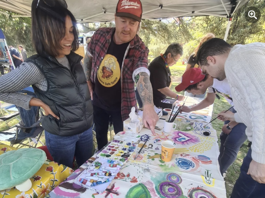 Five people are hovering around a pop-up table, painting on a sheet. 