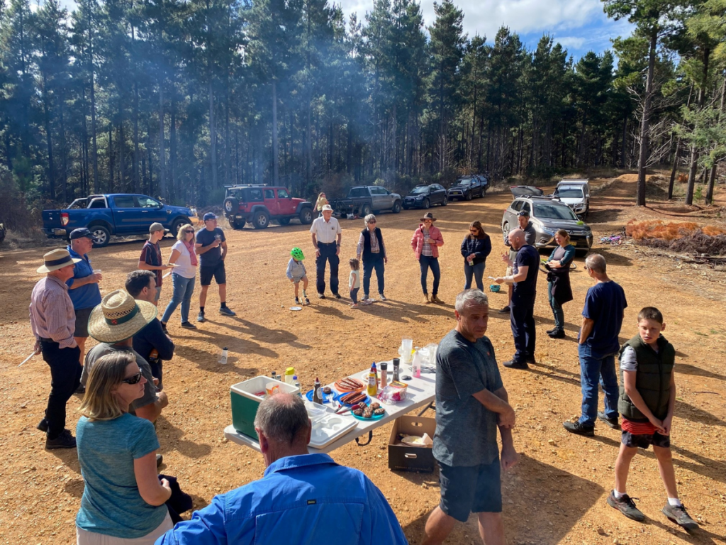 Group of people gathered for an event in a clearing surrounded by trees. 