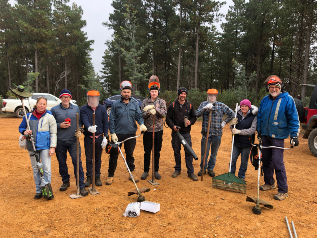 A group of people stand together with various tools, smiling for the camera. 