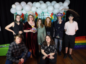 Group of young people celebrating, with a balloon garland behind them.