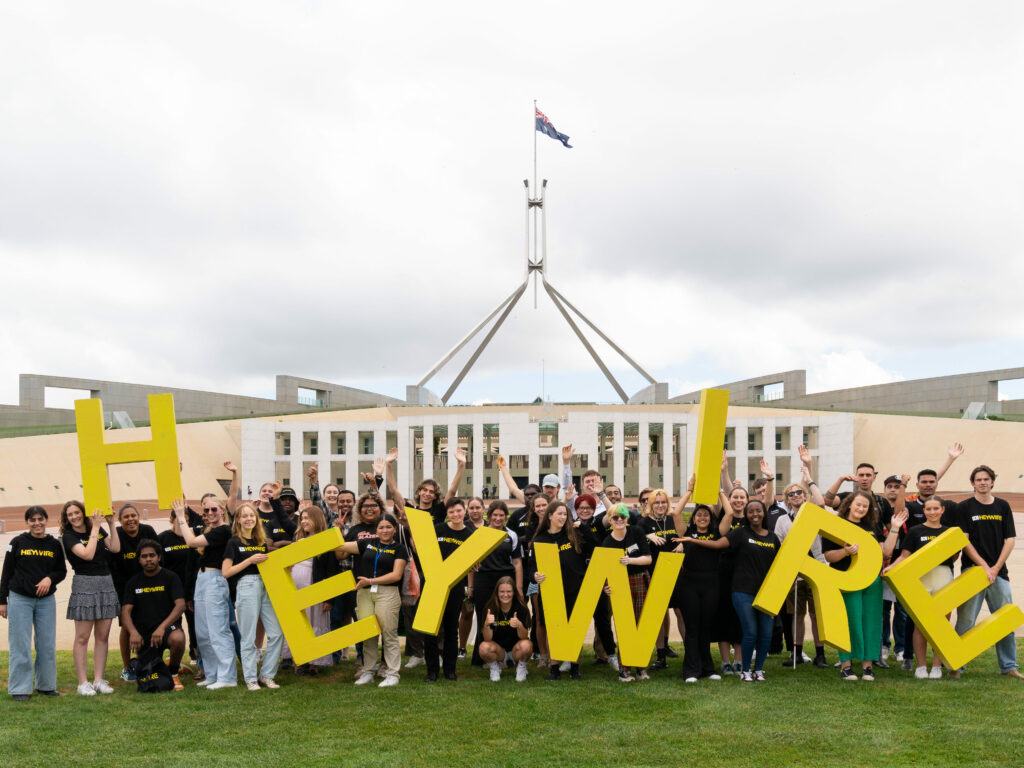 2024 Heywire participants in front of Parliament House in Canberra, holding up individual letters to spell HEYWIRE