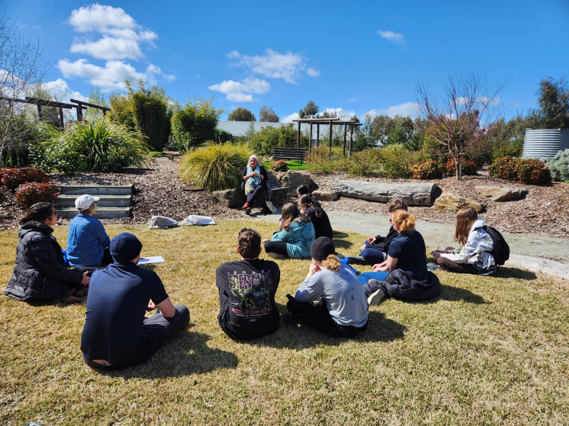 Students sitting in on the ground in an outdoor education lesson.