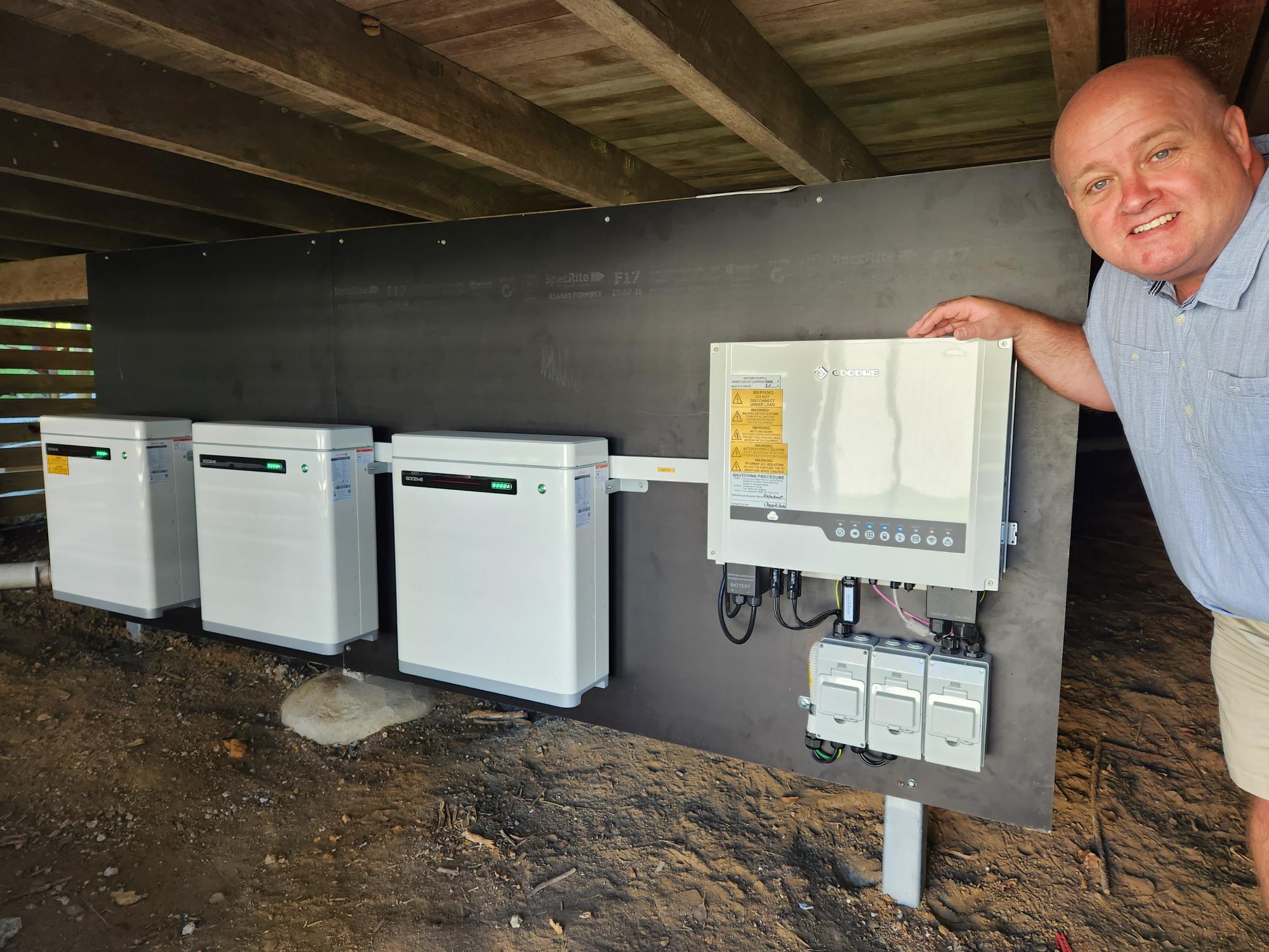 Jason Carroll standing next to three batteries installed at Mooloolah Valley Community Association Inc