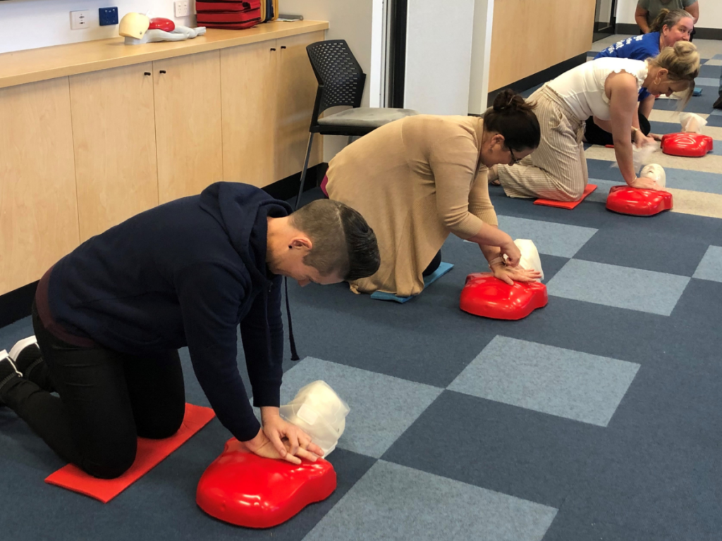 Three people crouched down on the floor practicing CPR on red dummies.