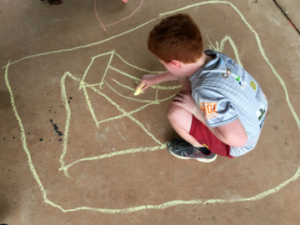 Child crouched on ground drawing with chalk on concrete.